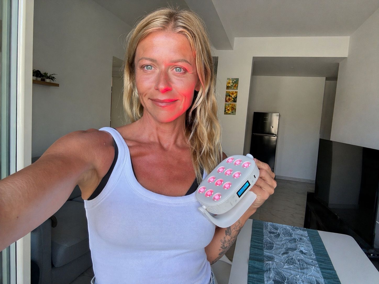 Woman holding a device with red light,  a skincare or wellness device, in an indoor setting.